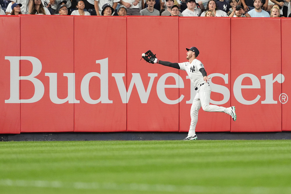 Yankees left fielder Cody Bellinger reaches as far as he can with his glove to catch a ball right in front of the Budweiser sign in left field in Yankee Stadium
